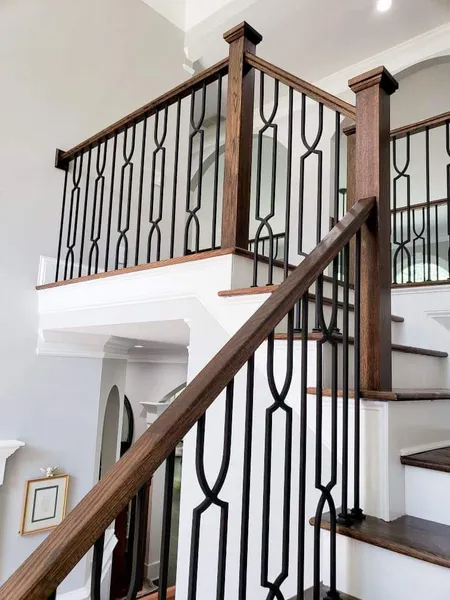 Staircase with wooden handrails and dark metal balusters. White walls, wood steps, and a landing.