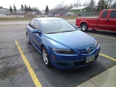 A blue car is parked in a parking lot next to a red truck