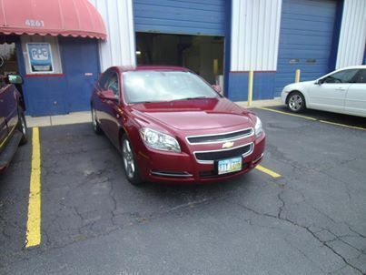 A blue car is parked in a parking lot next to a red truck