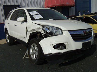 A white suv with a damaged front end is parked in front of a building.