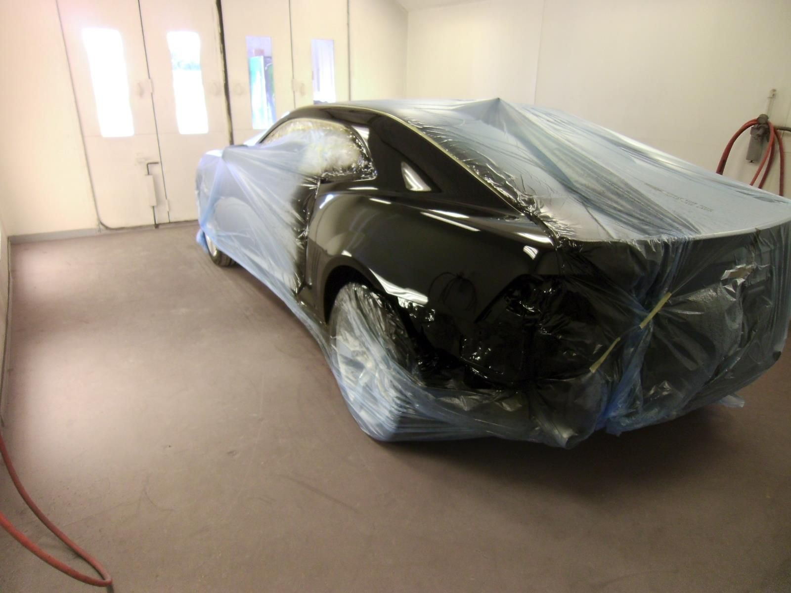 A black car is wrapped in plastic in a paint booth