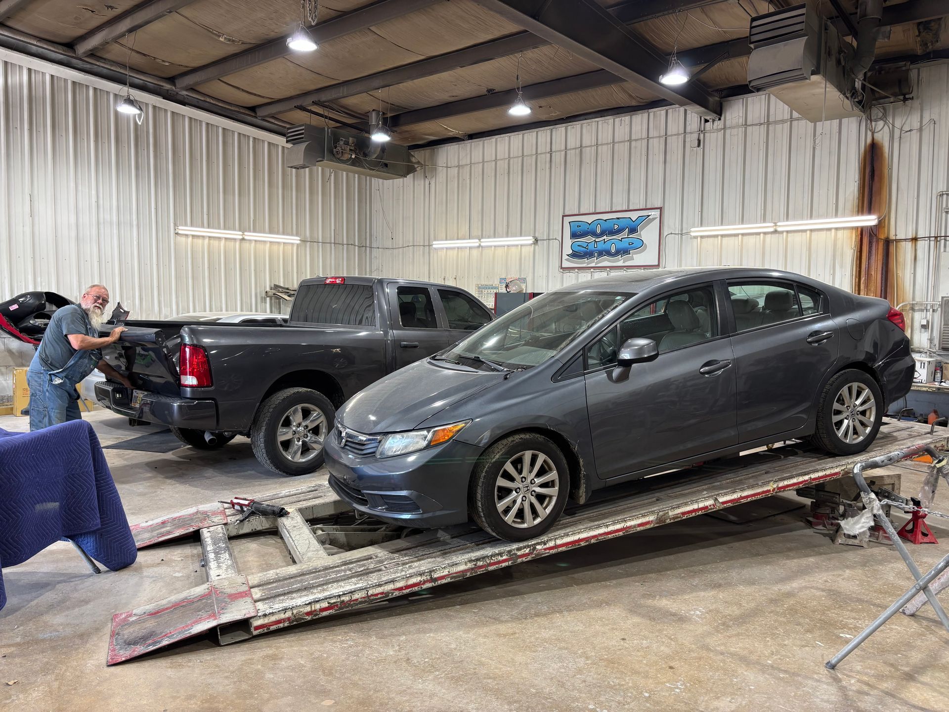 A car is sitting on a ramp in a garage next to a truck.