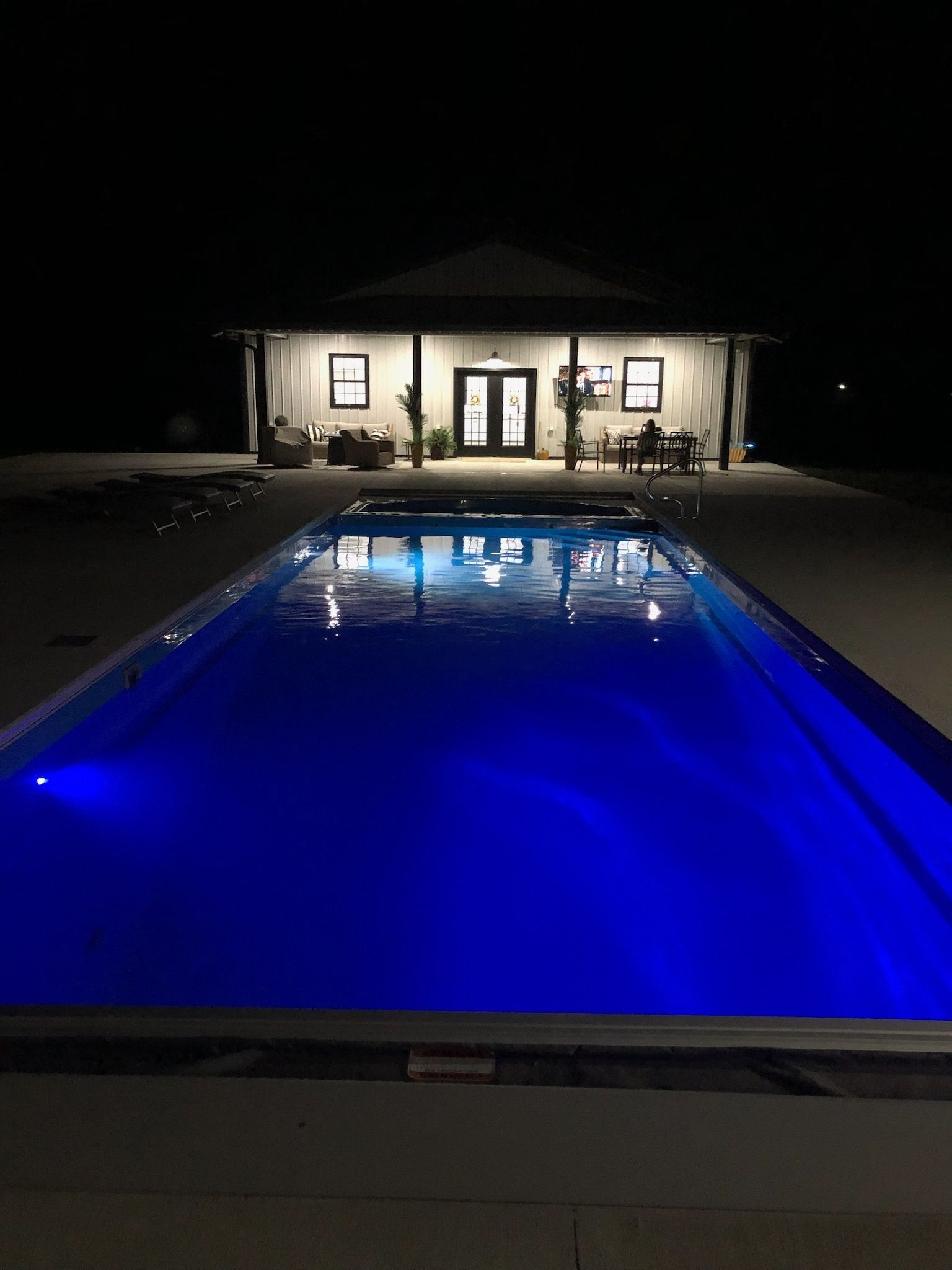 A large swimming pool is lit up at night in front of a house.