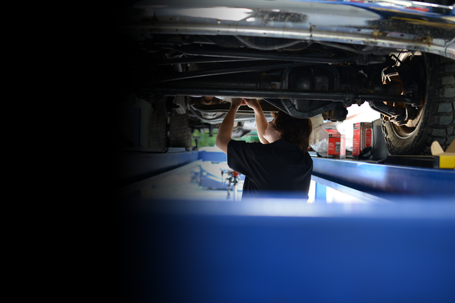 Mechanic working under a car on a lift in a dim auto shop