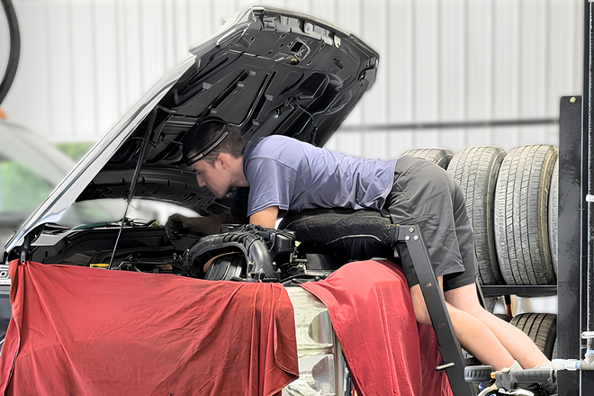 Mechanic inspecting engine with hood open on a car in a garage