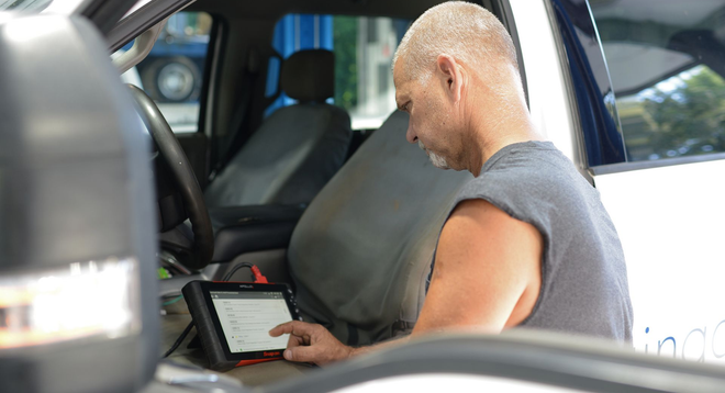 Person using a laptop in a car interior, viewed from the side.