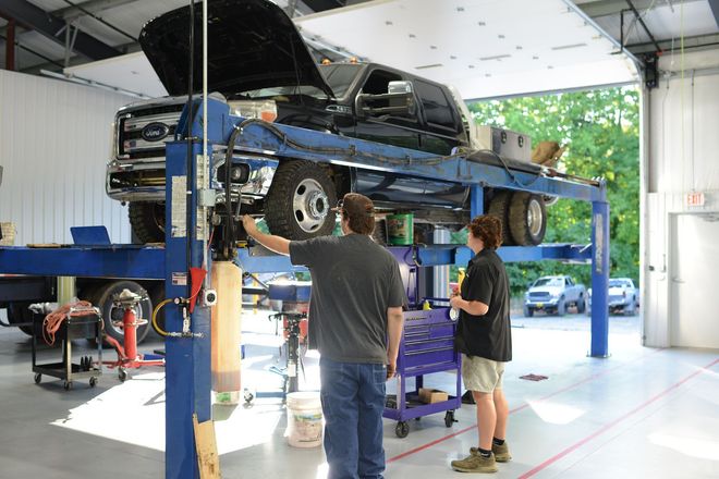 Car lifted on a blue auto hoist while two people inspect it inside a garage