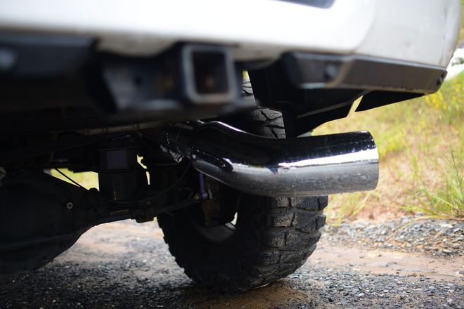 Close-up of a pickup truck’s rear exhaust pipe over a gravel road with grass nearby