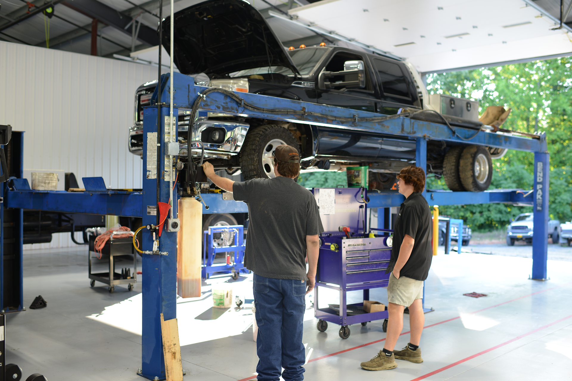 Blue car lifted on a garage hoist while two people inspect it in an auto repair shop