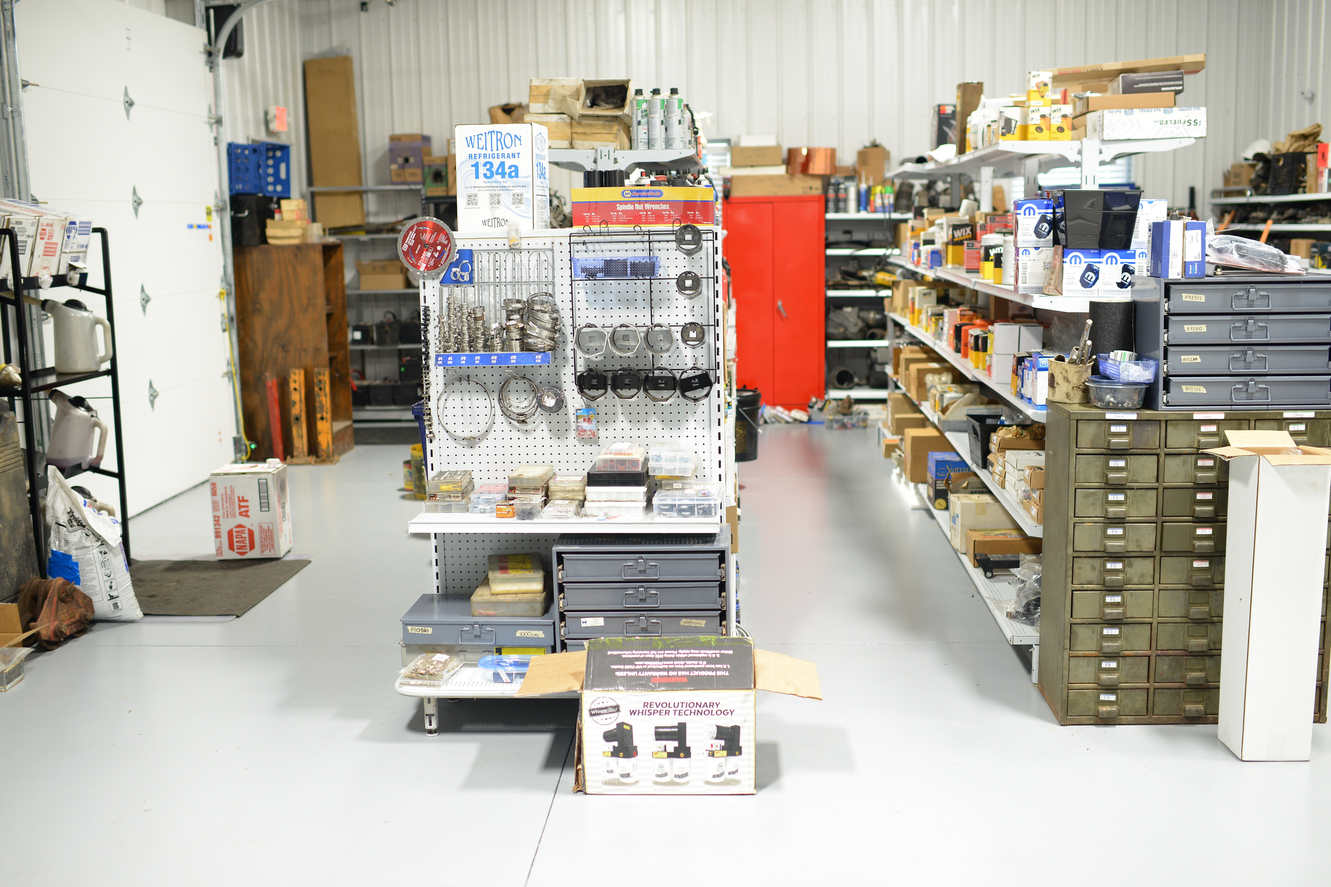 A cluttered hardware or storage room with shelves of tools, supplies, and stacked bins.