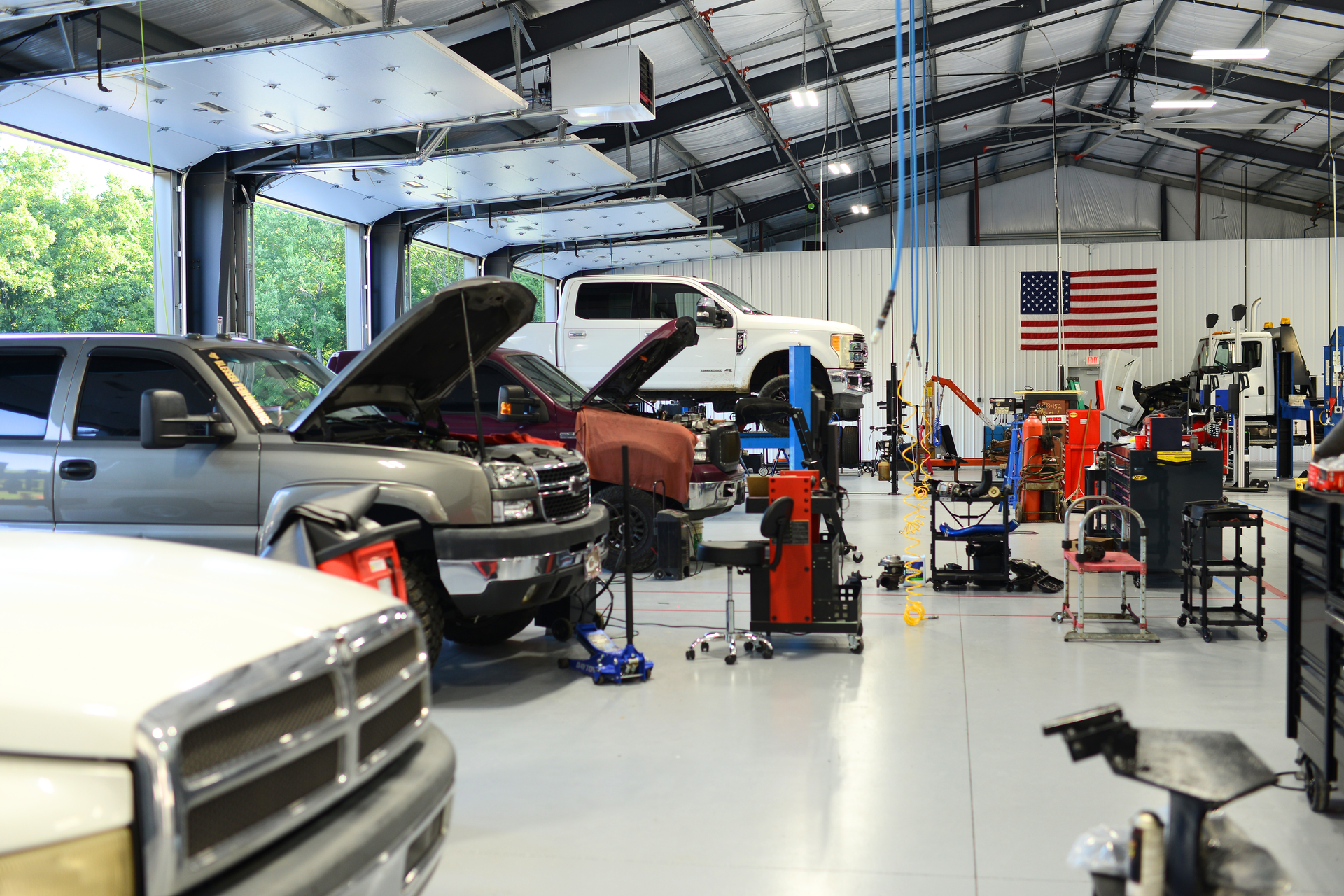 Auto repair shop with several vehicles, including a truck with its hood open, and tools in a bright garage