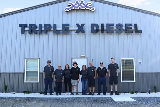 People standing outside the Triple X Diesel building in front of a blue metal facade