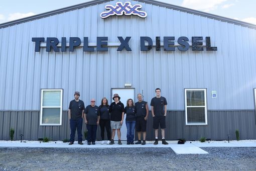People standing outside the Triple X Diesel building in front of a blue metal facade