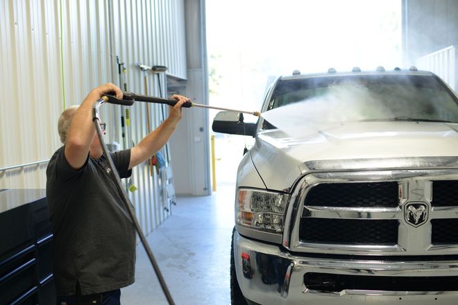Worker pressure-washing a white Dodge truck in a car wash bay