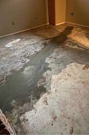 Water-damaged concrete floor in a room, with a large, dark water stain across the surface.