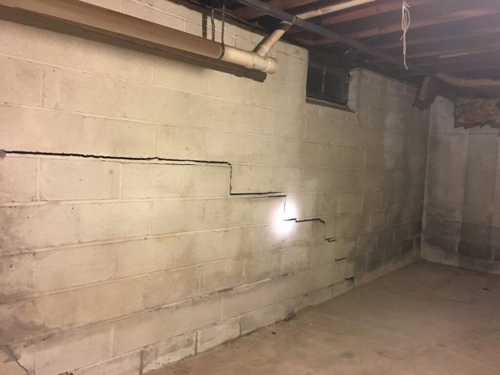Cracked concrete block basement wall; dark with potential water damage and window.