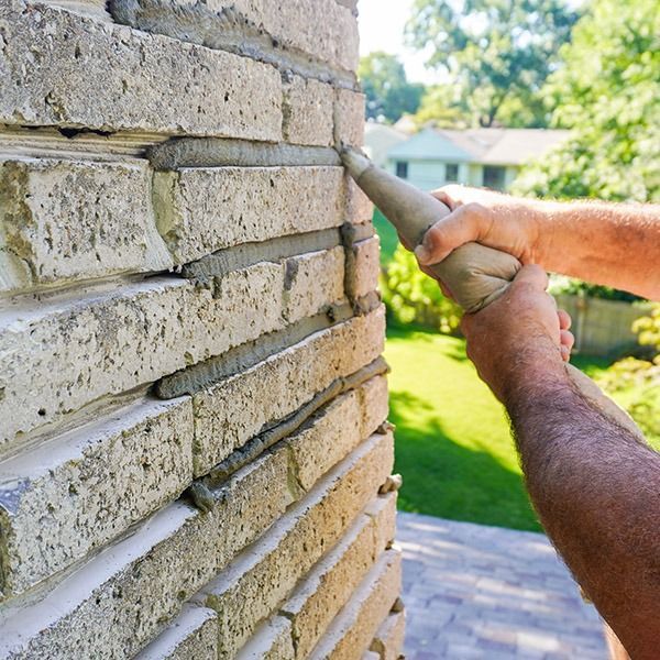 Man applying mortar to brick joints with a grout bag. Outdoor setting with a green lawn.