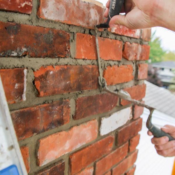 A person repointing a brick chimney with mortar and a trowel, outdoors.