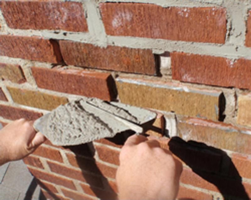 Person using a trowel to apply mortar into a brick wall joint.