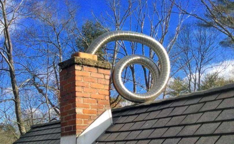 Brick chimney with a silver, spiral-shaped exhaust pipe against a blue sky.
