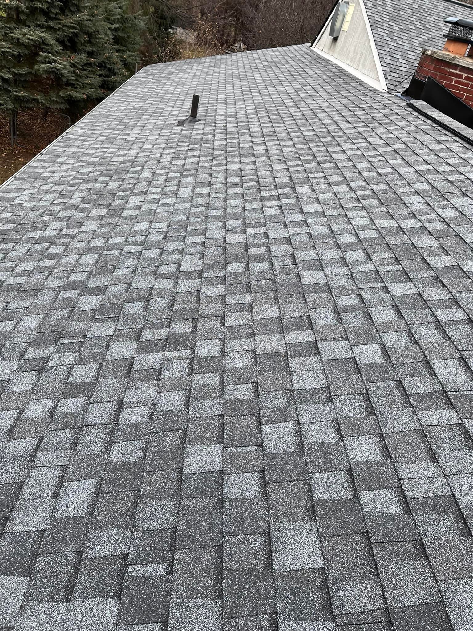 View of a gray asphalt shingle roof, showing wear and a vent pipe.