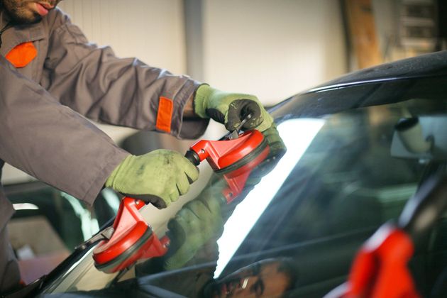 Person cleaning a car windshield with a red cloth and spray bottle on a rainy day.