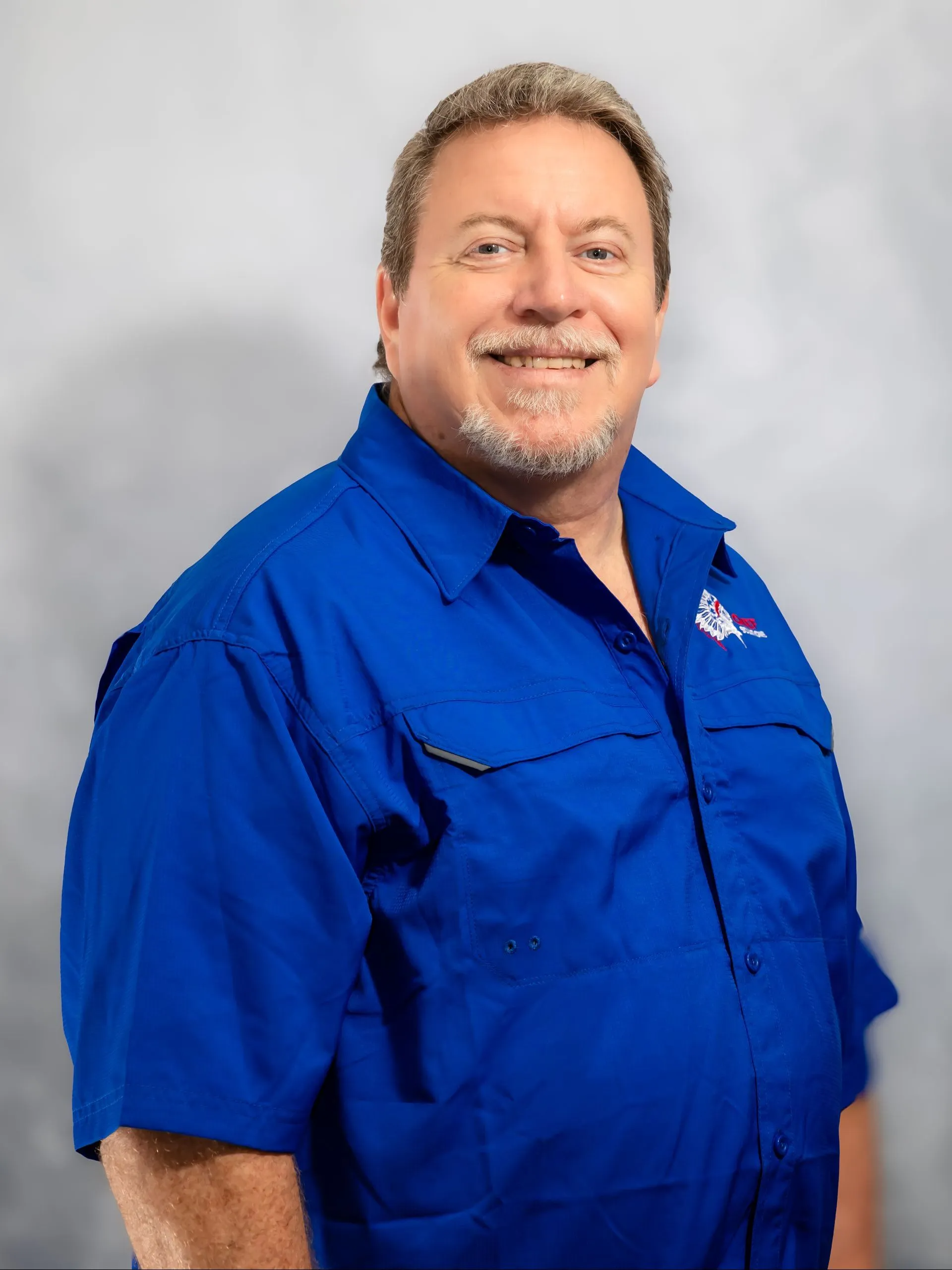 Man in blue shirt smiles, facing slightly to the side against a grey backdrop.