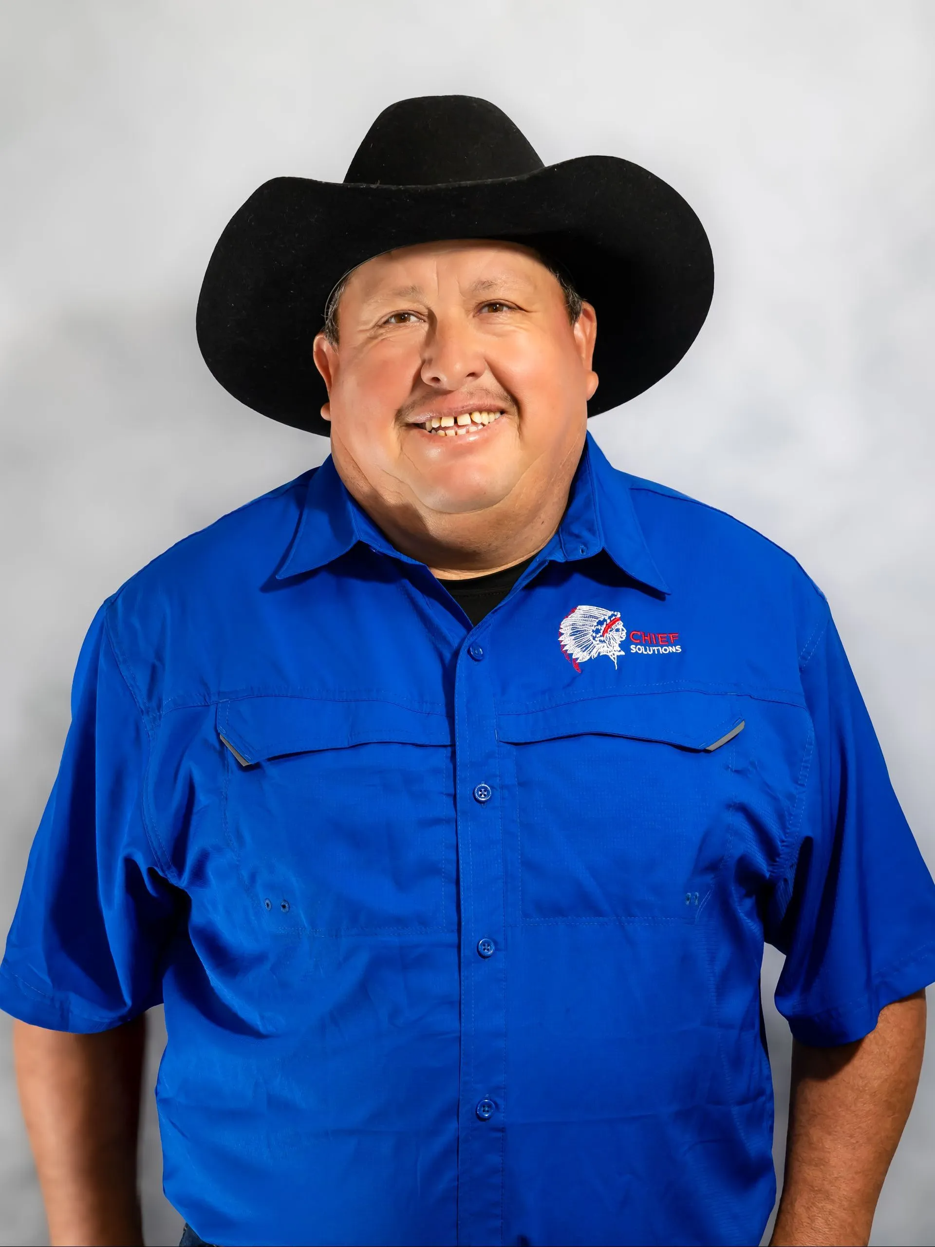 Man in cowboy hat and blue shirt smiles, posing against a light gray backdrop.