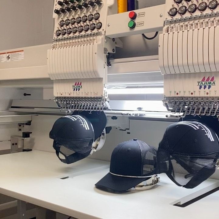 Embroidery machine stitching black hats on a worktable in a factory setting