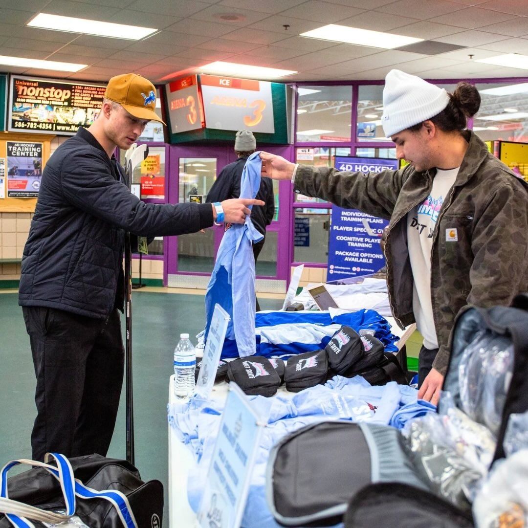 Two people exchanging a blue-and-white shirt at a retail table display.