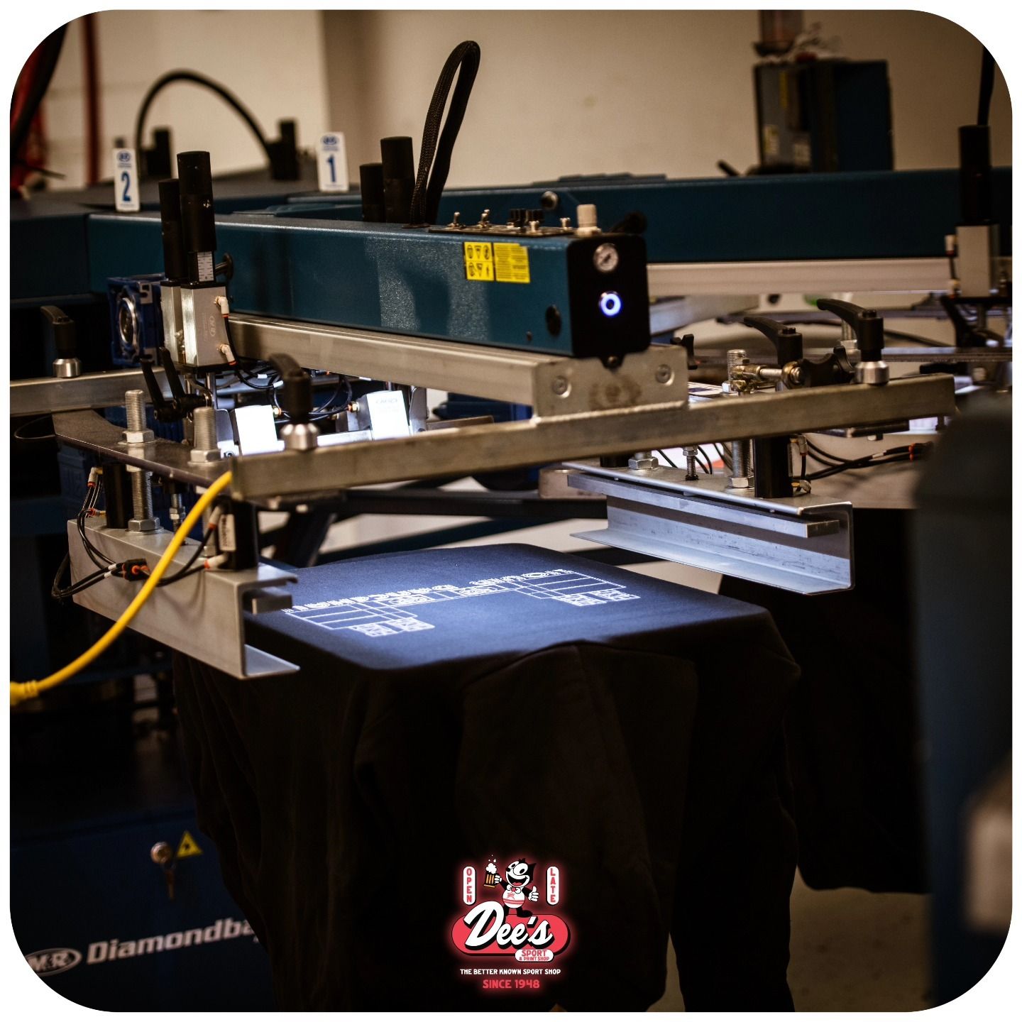 Screen-printing press printing a black T-shirt with a white design on the platen