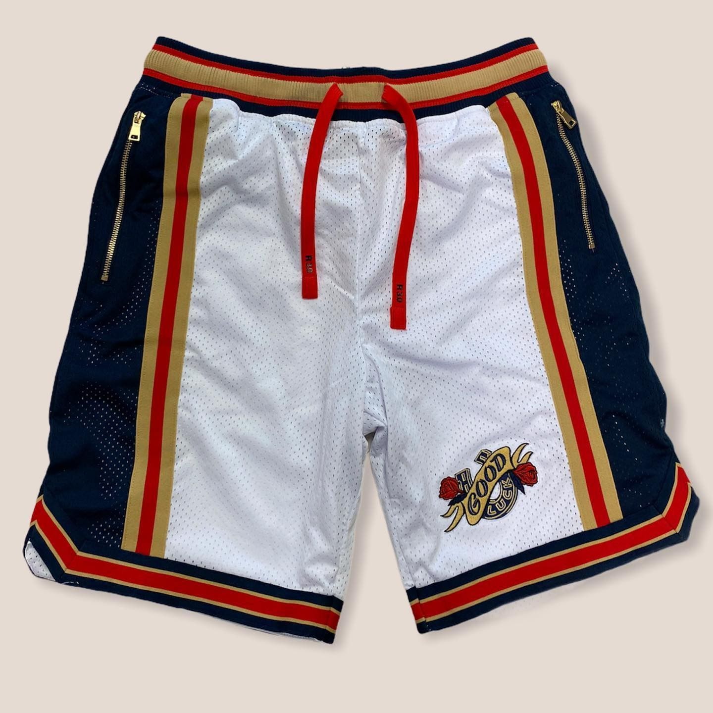 White athletic shorts with navy, red, and gold side stripes and a red drawstring, laid flat.