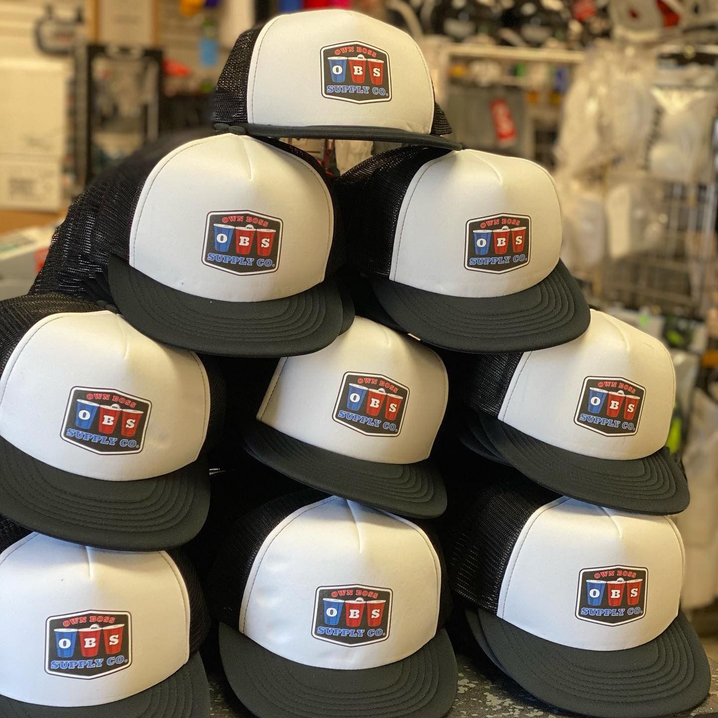 Stacked black-and-white trucker hats with a small colorful patch, displayed in a store.