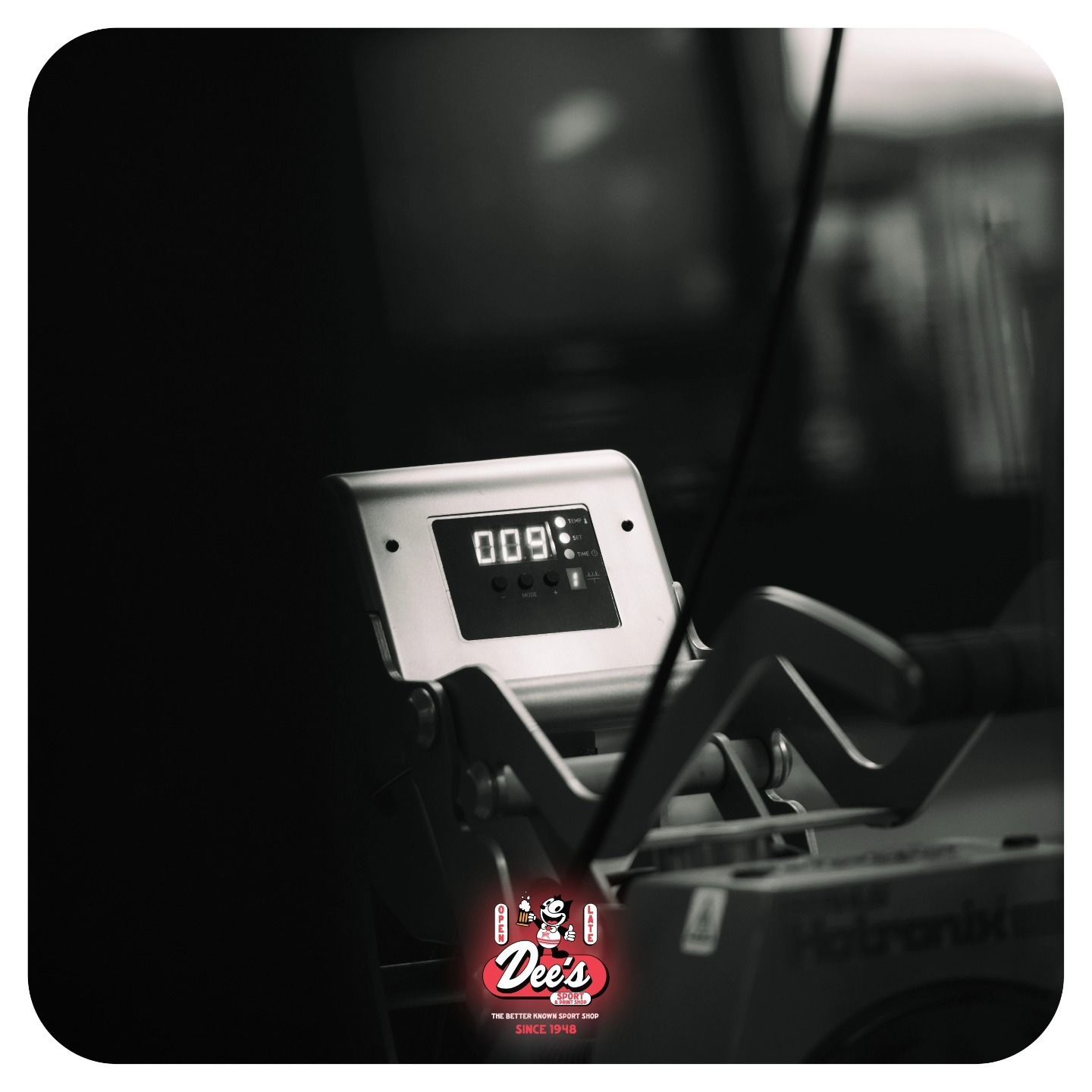 A digital exercise machine with a black-and-white display in a dim gym setting.