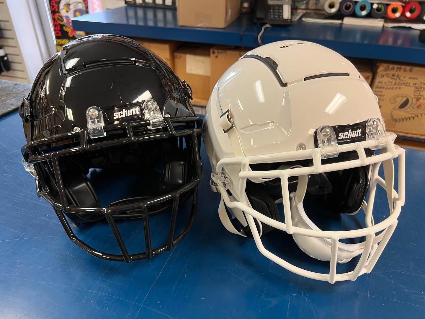 Two football helmets, black and white, sitting side by side on a blue table in a workshop.