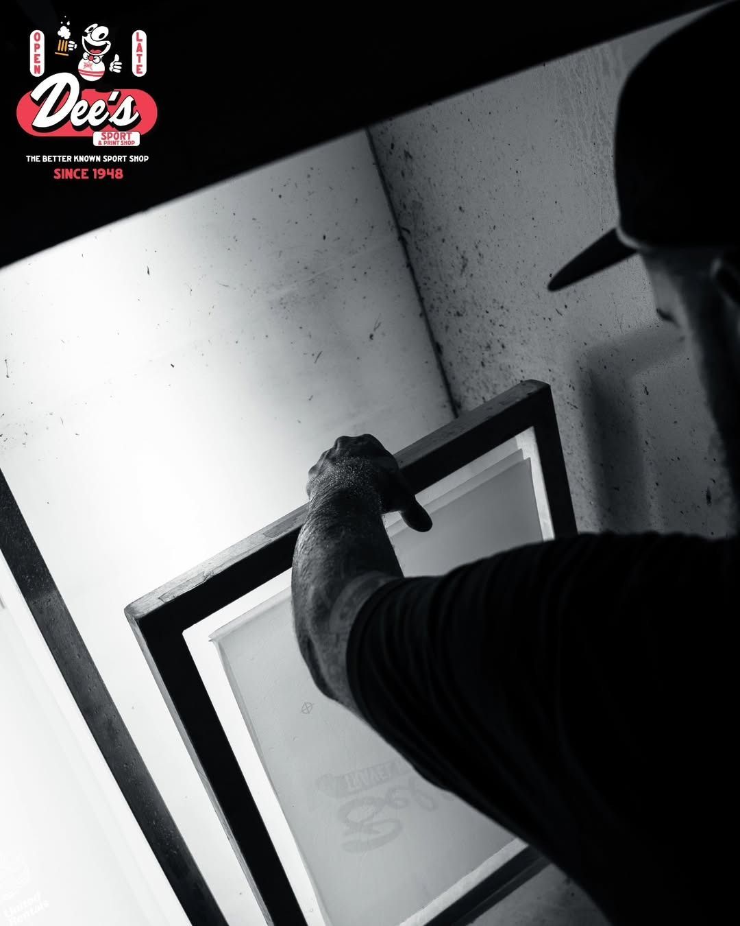 Person in a dark cap and shirt framing a white board on a wall in a black-and-white room