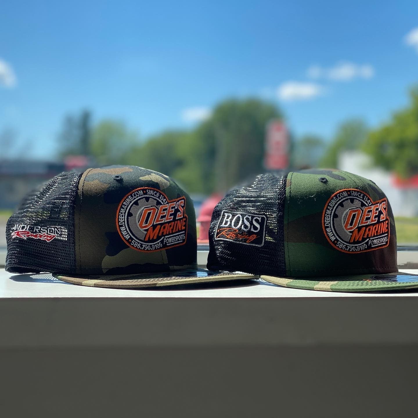 Two black and green mesh caps with orange logos on a table outdoors under a blue sky