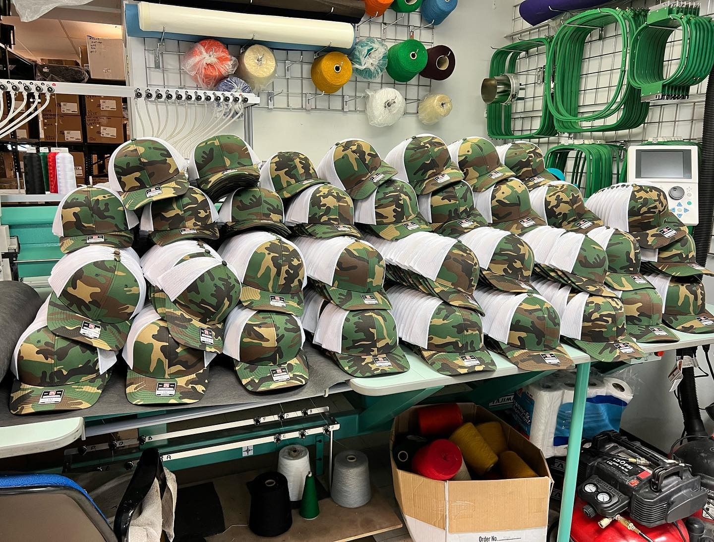 Stacks of camouflage helmets on a worktable in a gear shop, with ropes and equipment hanging behind them