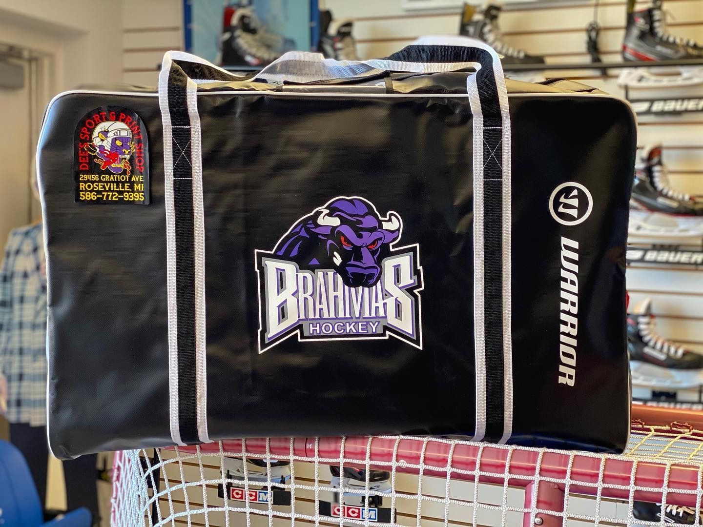 Black hockey equipment bag with purple Bruins logo and Warrior branding on a netted shelf