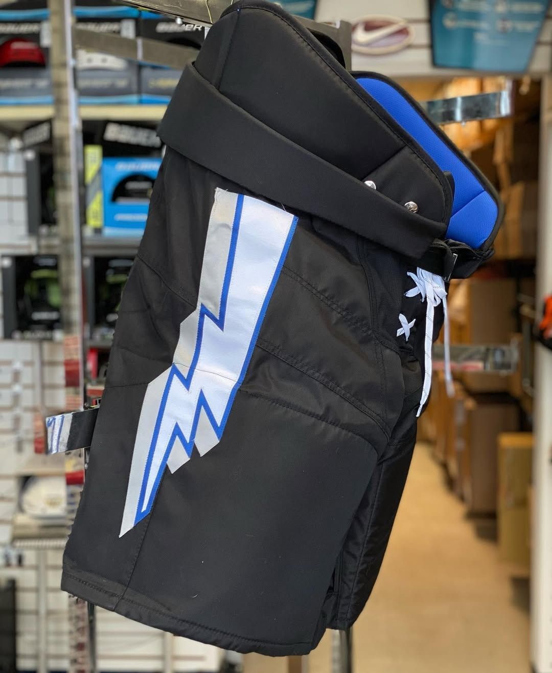 Black-and-blue padded hockey bag with a white lightning bolt design hanging in a sports store