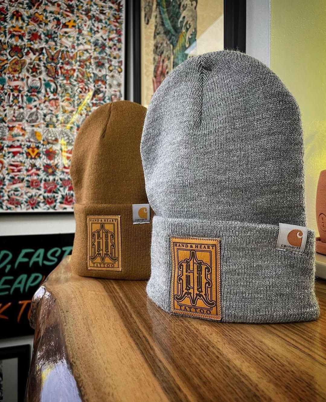 Two knit beanies, brown and gray, displayed on a wooden table by a window.