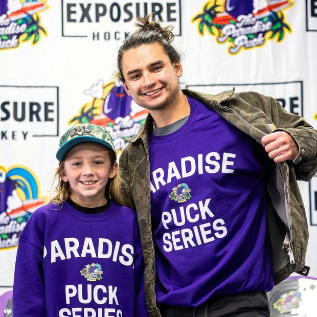 Two people in purple “Paradise Puck Series” shirts posing at an event backdrop