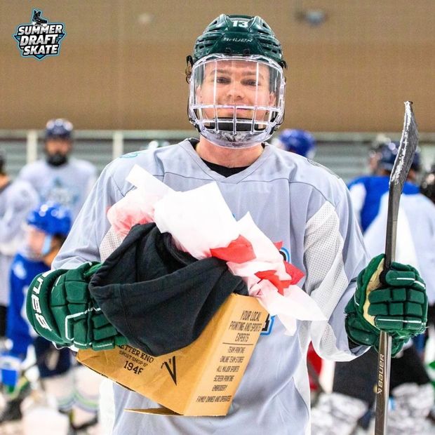 Ice hockey player in green holding a stick and a bundle of papers on the rink, smiling in helmet and gear