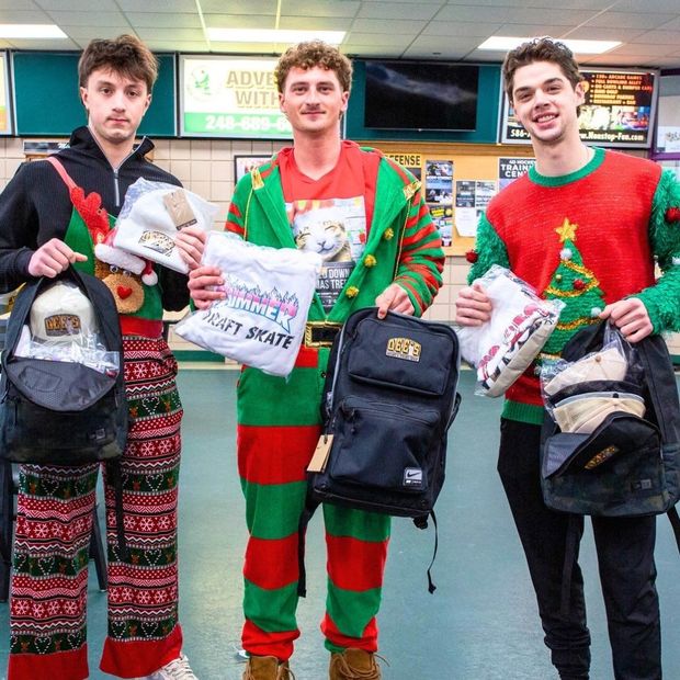 Three men in festive red and green outfits holding Christmas gifts and backpacks in a store aisle
