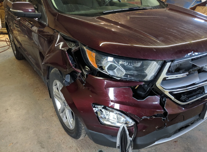 Damaged maroon SUV with front-end collision and crumpled bumper in a garage