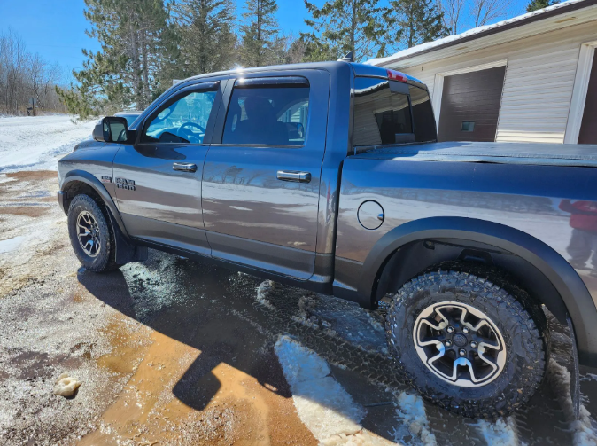 Blue and gray pickup truck parked on a snowy driveway beside a garage