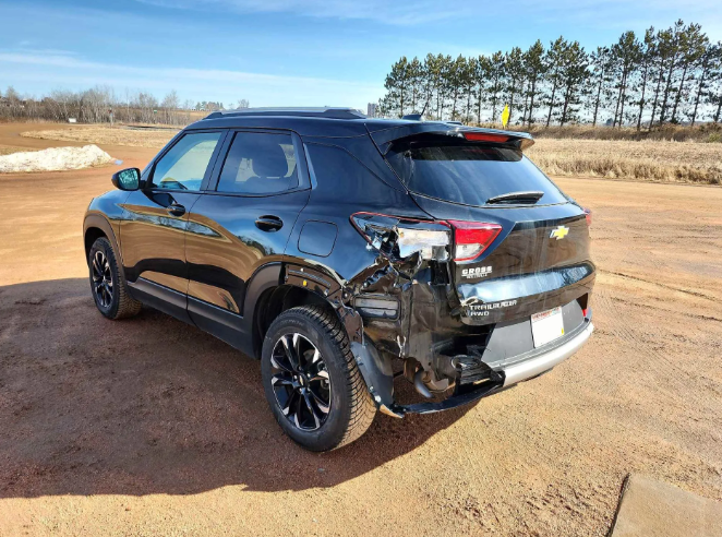 Black SUV with rear-side collision damage parked on a dirt road in a rural field