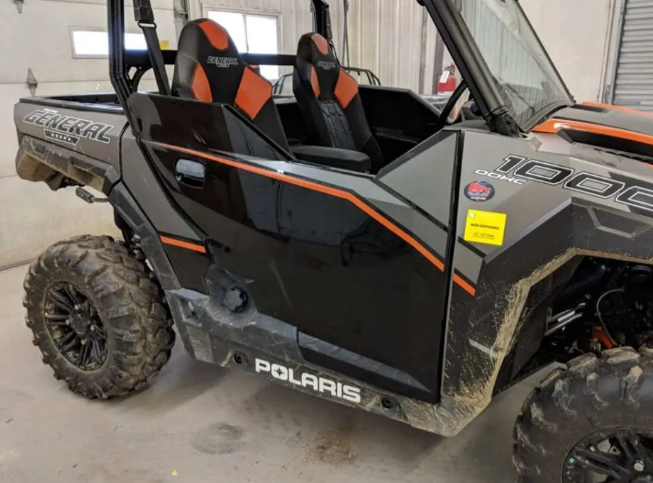 Black Polaris off-road UTV with orange accents parked indoors in a garage