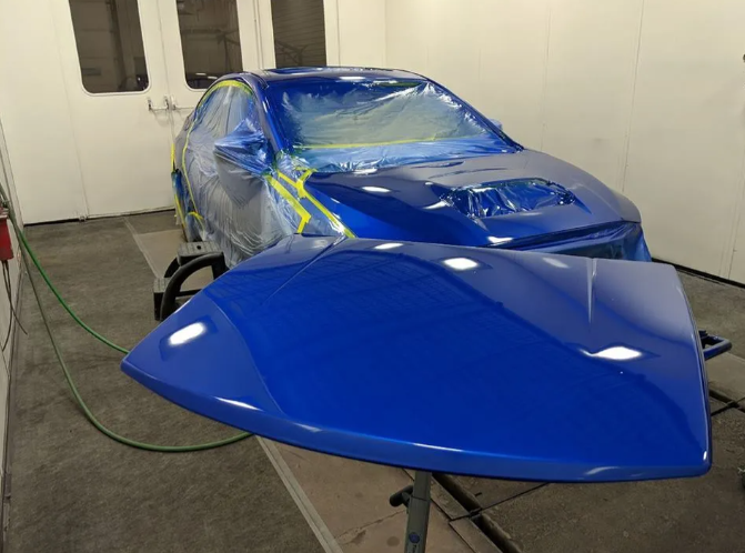 Blue car body parts taped and covered for painting in a workshop