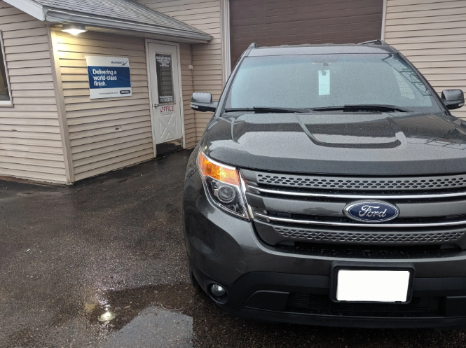 Gray Ford SUV parked beside a beige building with a garage door on a wet pavement